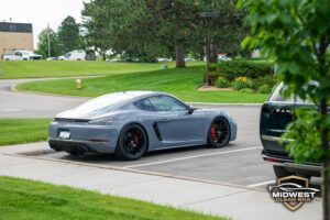 Gray Porsche Cayman after professional paint protection film (PPF), ceramic coating, and window tint installation, shown at a front three quarter angle with clear bra film protecting the hood, bumper, and fenders.