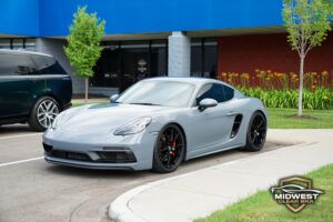Gray Porsche Cayman after professional paint protection film (PPF), ceramic coating, and window tint installation, shown at a front three quarter angle with clear bra film protecting the hood, bumper, and fenders.